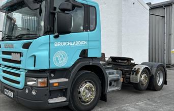 A Picture of a large lorry front cab decorated in Bruichladdichs turcoise blue with a Bruichladdich whisky distillery logo on it. It sits in front of
