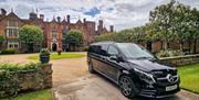 A black Mercedes luxury minivan parked in the driveway of a large manor
