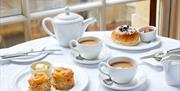 Two plates of food and two cups of tea and saucers next to a teapot