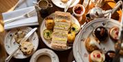 Overhead shot of sandwiches, small cakes, scones and tea on pretty floral china plates and cups.