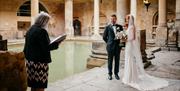 A celebrant wedding a couple in a ceremony alongside the Great Bath at The Roman Baths