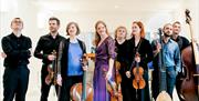 A group of people standing against a bright white background holding musical instruments