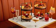 A small square table with a curved orange booth seating around it. The table has towered plates of fried food and chips along with five different cock
