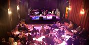 People sitting at individual tables in front of the stage at the Chapel Arts Centre in Bath
