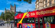 Red "Bath CitySightseeing" open-top bus with Bath Abbey visible in the background.