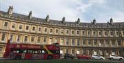 Red "Bath CitySightseeing" open-top bus parked in front of the Royal Crescent in Bath