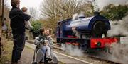 A family of four can be seen from behind waving at a blue steam train from the station platform.