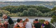 People sat on benches in a field with Chew Valley Lake in the background