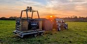 View of a basket that's being pulled by a truck parked in a field at sunrise, ready to be set up for take-off.