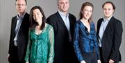 Three men and two women standing against a grey background