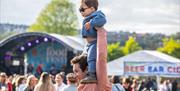 An image of a man holding up a young boy over his shoulders at the Foodies Festival.