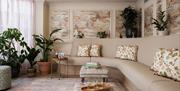 The lounge at Francis Hotel Spa, with a large curved sofa along the right and back wall and a full-length window on the left. Multiple potted plants l