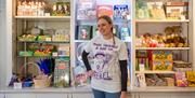 Person posing in front of shelves wearing a make trouble & rise up - rebel shirt with a someone holding a sign that says deeds not words.
