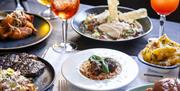 Plates of food with two Aperol Spritz drinks in the background on an indoor table at Green Park Brasserie