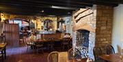 Dining room of pub with stone brick walls and fireplace and wooden tables and chairs.