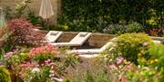 A line of cream sunbeds surrounded by Cotswold stone walls and pretty pink hues of flowers and plants.