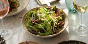 A light salad and other fresh looking Michelin level standard food on a white marble table with wine glasses.