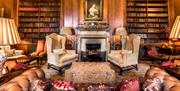 An old fashioned traditional wooden panelled library room with a framed oil painting above a stone fireplace and a chesterfield sofa and two sitting c