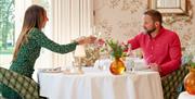 A couple toasting over a table with ornate background and wallpaper