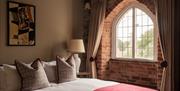 A double bed alongside an exposed brick wall with a large arched window and white curtains.