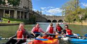 Photo of people, presumably on a bridal party given the attire, in kayaks in the river Avon near the Parade Gardens on a sunny day in Bath