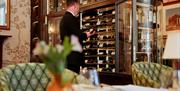 A waiter in a black jacket choosing wine from a large glass fronted fridge.