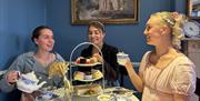 Three women having afternoon tea while dressed in period costume at the Regency Tea Room inside The Jane Austen Centre in Bath.