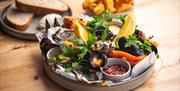 A plate of Surf 'N' Turf with sides of sourdough bread and chips in the background at The Scallop Shell in Bath