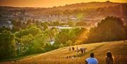 Scenic backdrop of people sitting on a hill in the late afternoon/early evening looking down at the city of Bath
