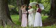 Three women standing between trees wearing period dress