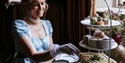 A woman eating afternoon tea while wearing period dress