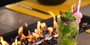 A cocktail sitting on a table next to a flaming grill.