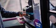 A person scanning their phone on a tap on-tap off reader aboard a bus in the West of England