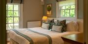 A country style bedroom with creams and light jade colourways, a double bed and two windows with roman blinds.