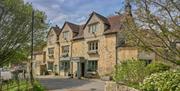 A Cotswold stone building on a country road with trees surrounding it.