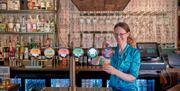 Marianne (pub owner) in a blue shirt pulling a pint of ale behind a pub bar.