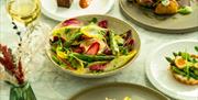 Plates of colourful salads and Spring feeling Michelin-level food on a white marbled table along with a glass of white wine.