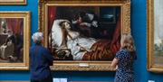 Two people looking at a painting in the Upper Gallery at the Victoria Art Gallery in central Bath, UK.