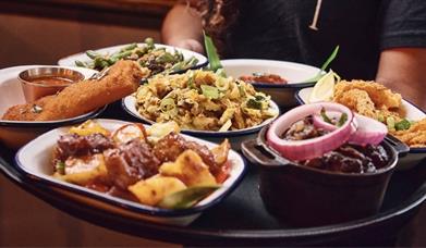 Seven plates of Sri Lankan food on a small table with someone sitting in the background.