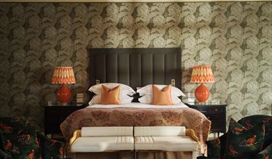 Jacuzzi in a mood-lit hotel bedroom with some comfortable seating and champagne on a table in front of it.