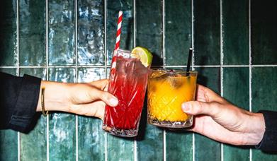 two people cheersing a red and oragne cocktail