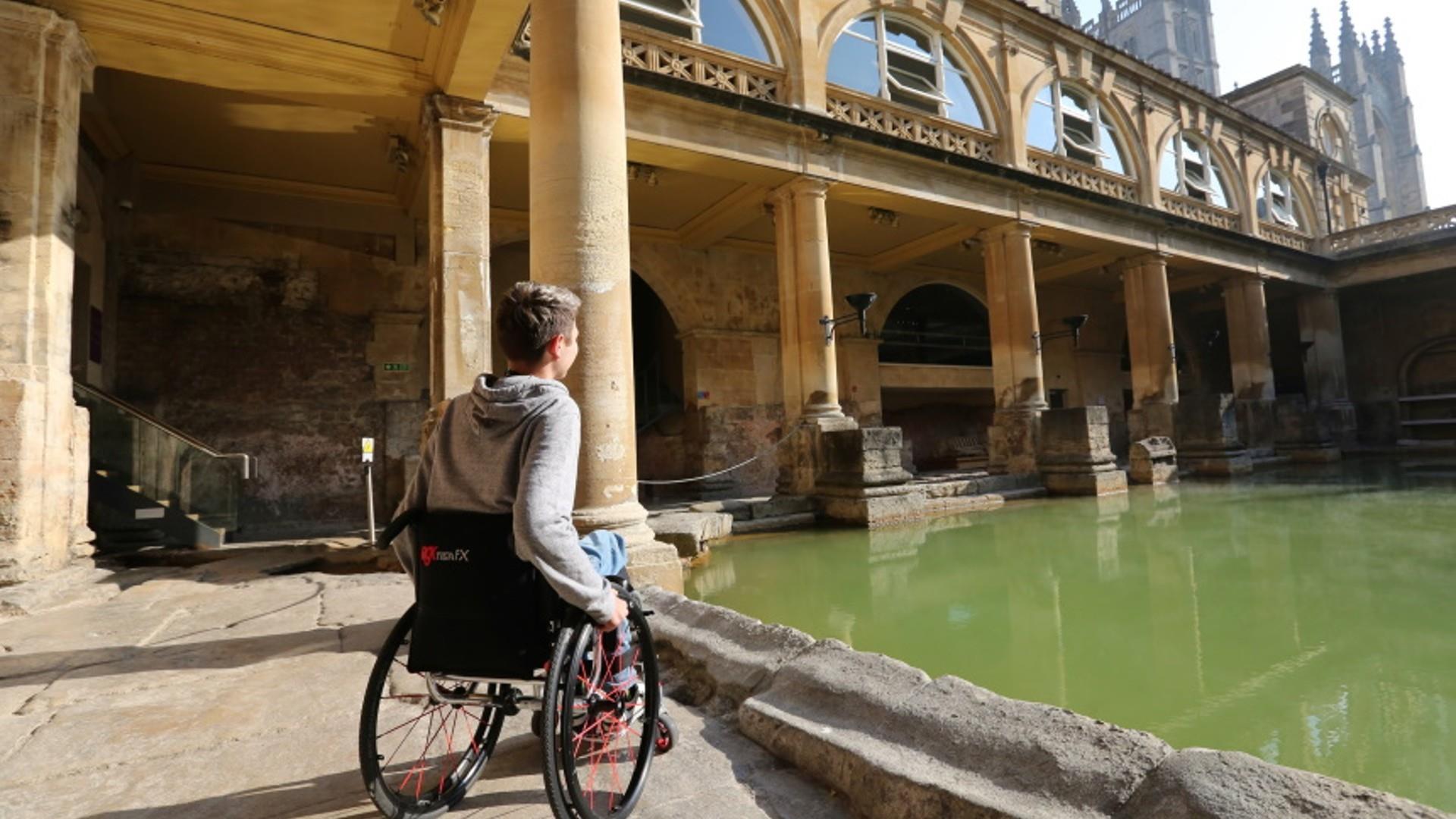 A man in a wheelchair looks out over The Roman Baths