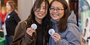 Two women holding handmade badges at the World Heritage Day event in Bath's Guildhall