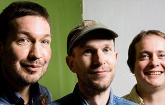Three men posing for a photograph against a green and white backdrop
