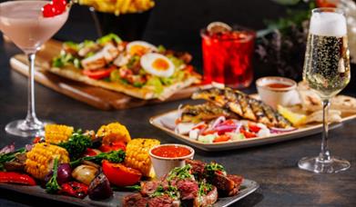 Image shows an assortment of dishes available as part of the Bottomless Brunch. A cocktail and glass of Prosecco are positioned either side.