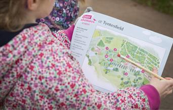 A girl in a pink floral coat looking at a map of Tyntesfield