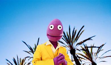 Randy Feltface in a yellow suit standing against a sunny background. 