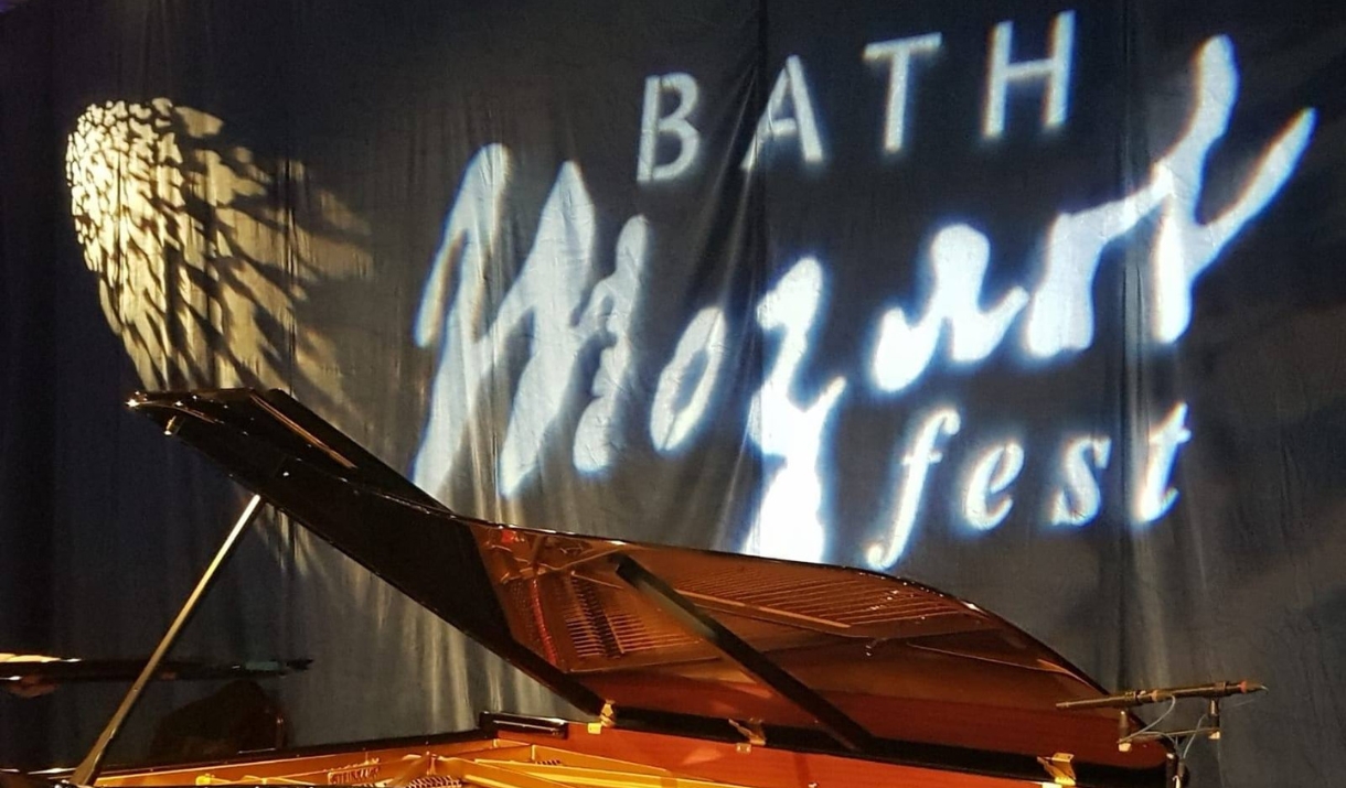 A piano on a stage with the words 'Bath Mozartfest' projected on to a curtain in the background