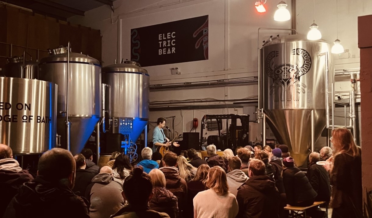 Person playing guitar in fromt of audience in brewery