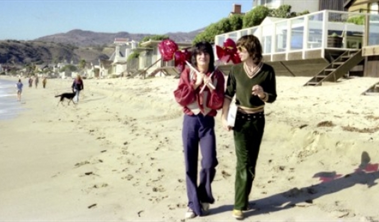 Ronnie Wood and Mick Jagger walking along a beach.